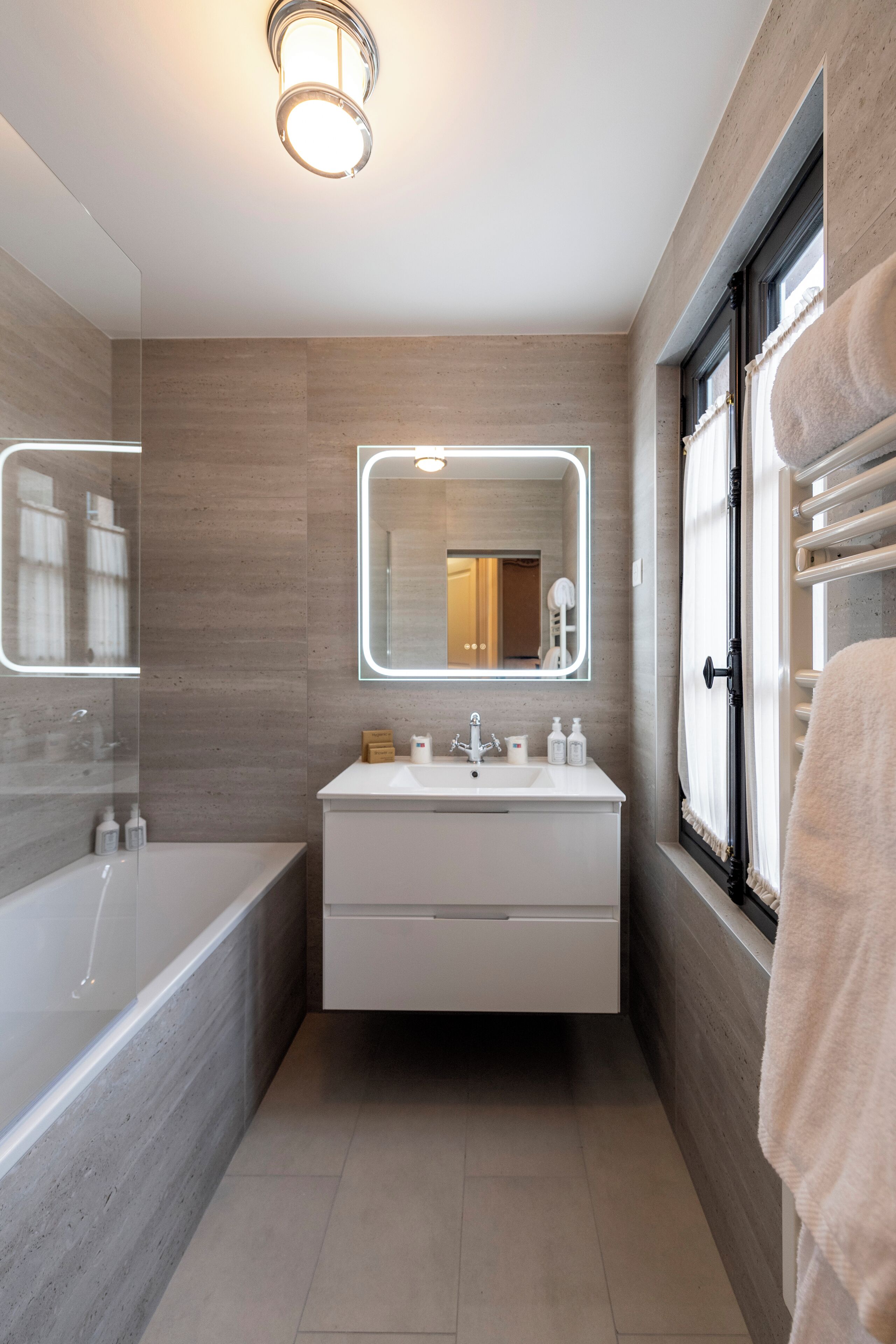 Un baño moderno con una bañera grande, un tocador con espejo y una ventana con una toalla colgando.