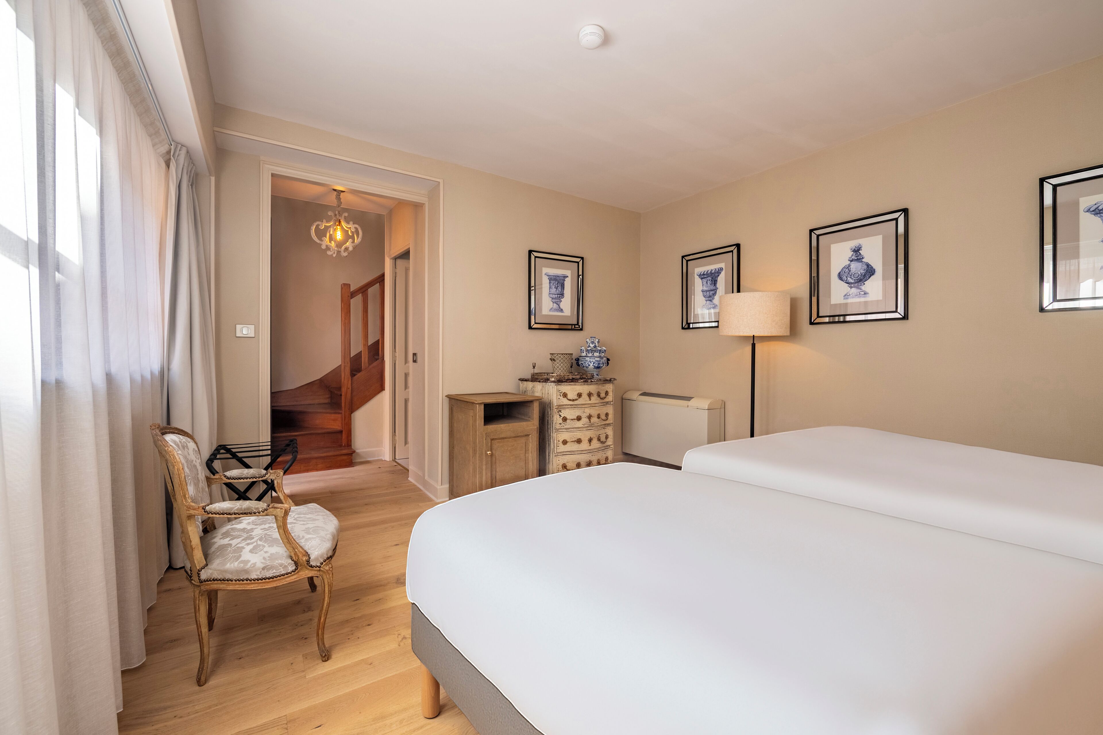 A hotel room with a large bed, a wooden chair, a dresser, and framed artwork on the walls.