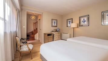 A hotel room with a large bed, a wooden chair, a dresser, and framed artwork on the walls.