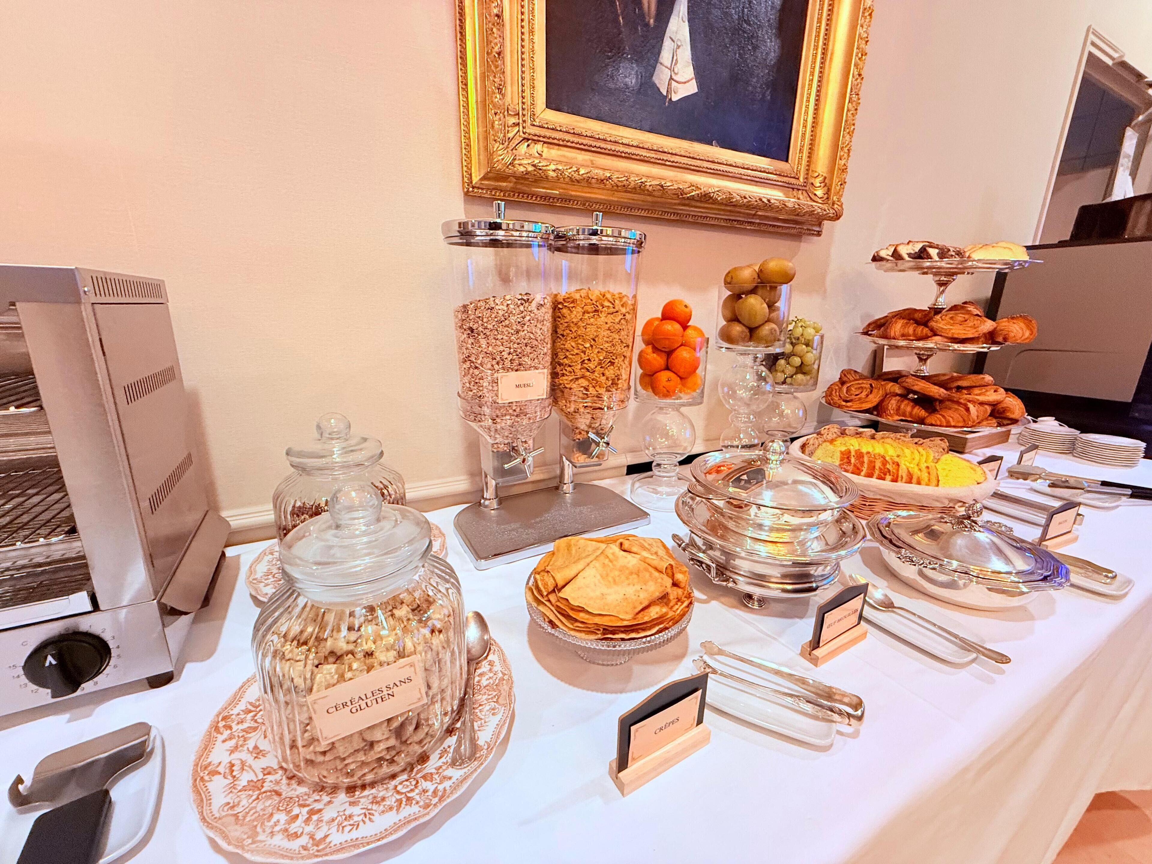 A buffet table with various food items, including cereals, fruits, pastries, and a painting on the wall.