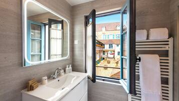 Un bagno moderno con uno specchio grande, un lavandino bianco e una finestra che si affaccia su un cortile.