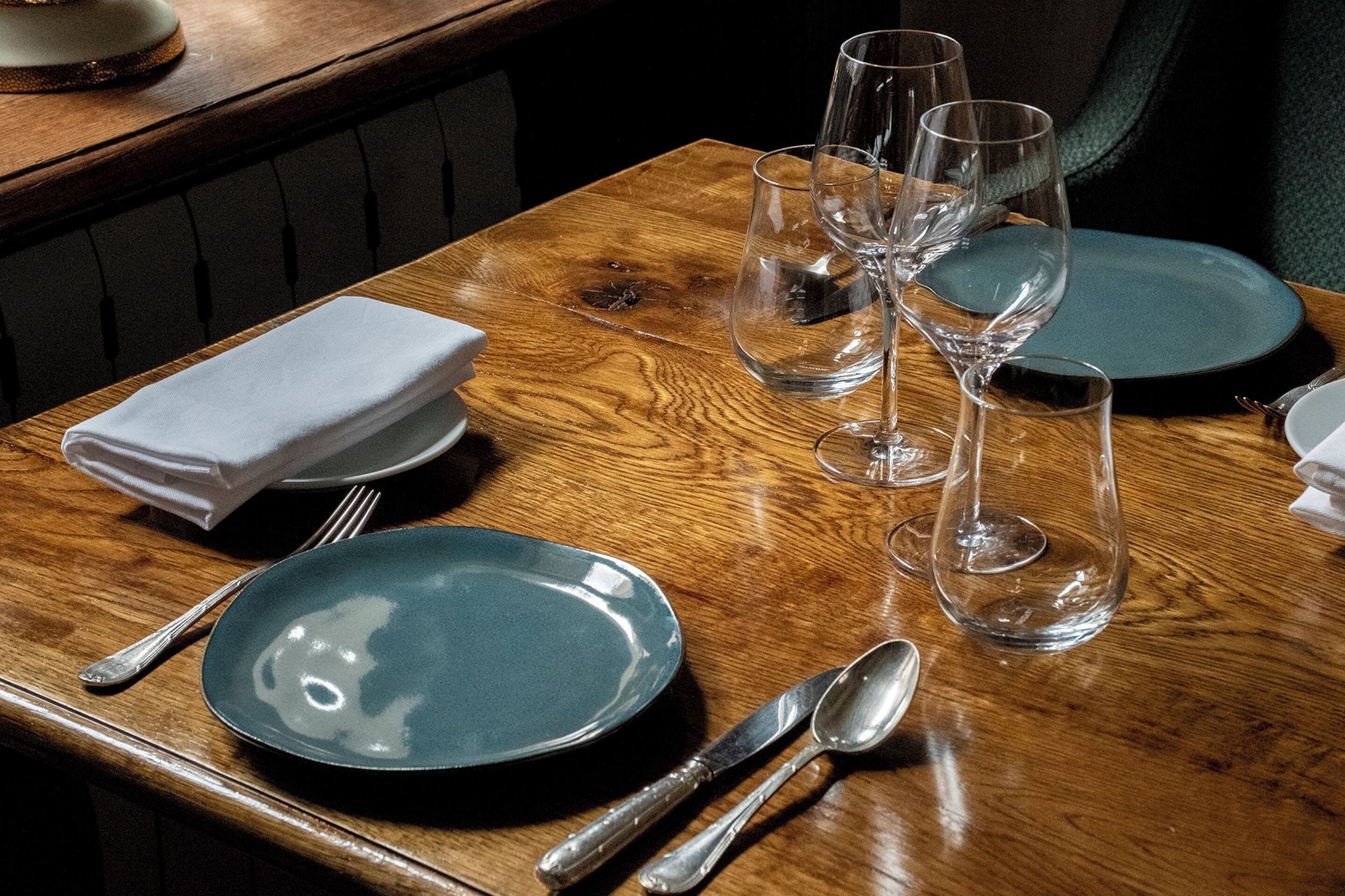 A neatly set dining table with a green plate, silverware, and multiple wine glasses.