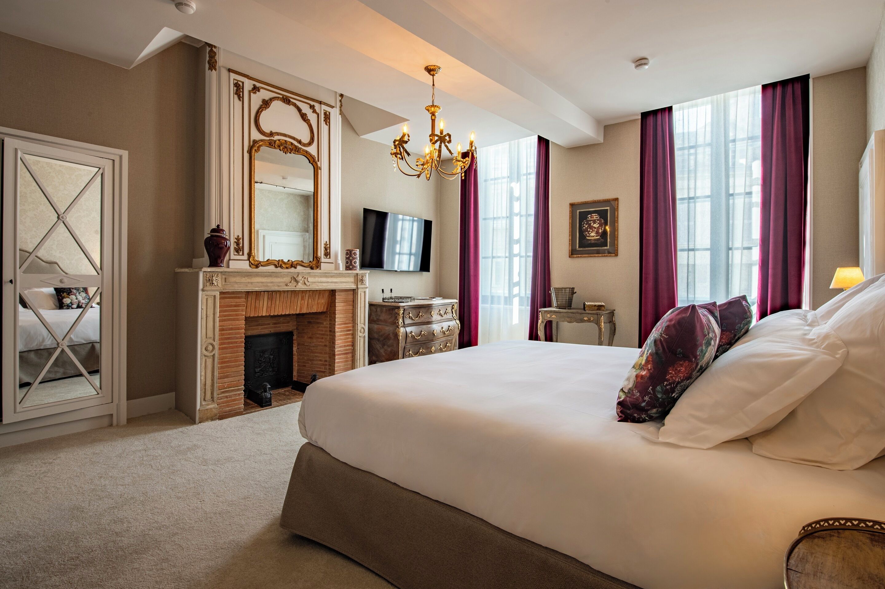Een ruime slaapkamer met een groot bed, een open haard, een televisie en een spiegel.