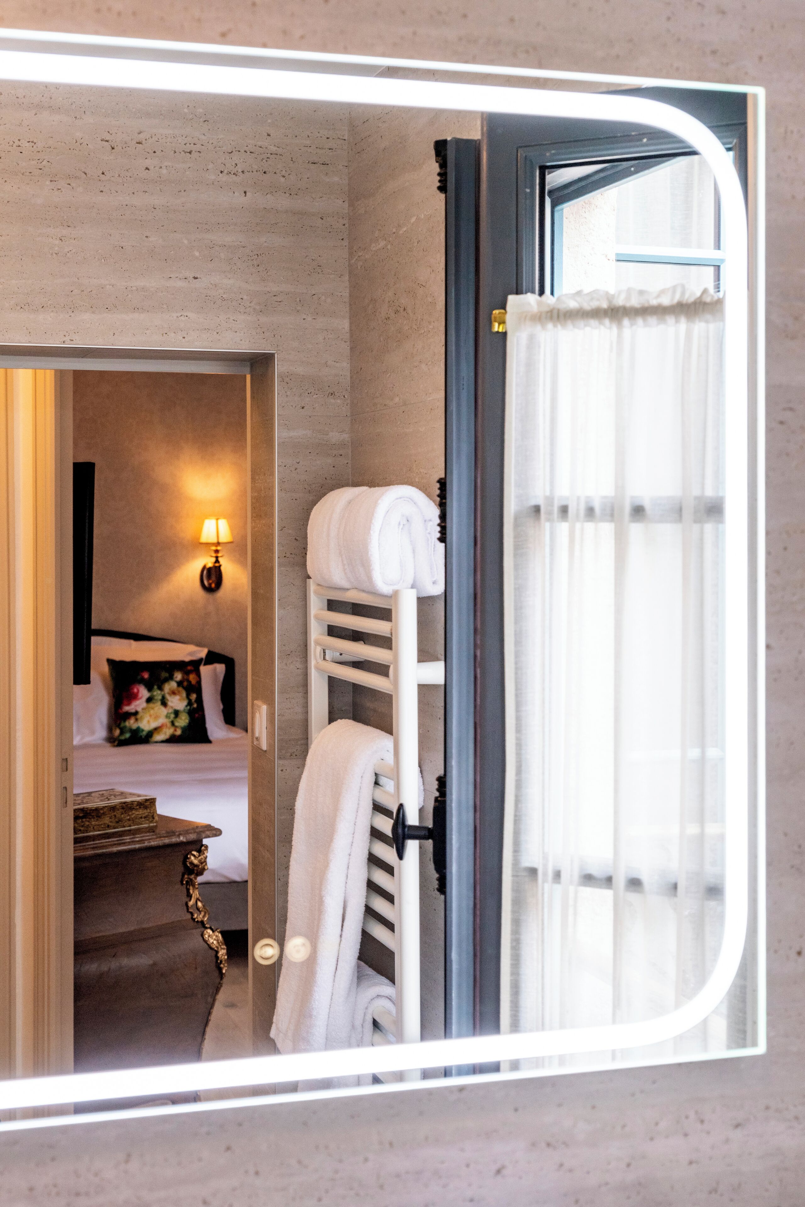 Een hotelkamer met een bed, nachtkastje, lamp en handdoekrek.