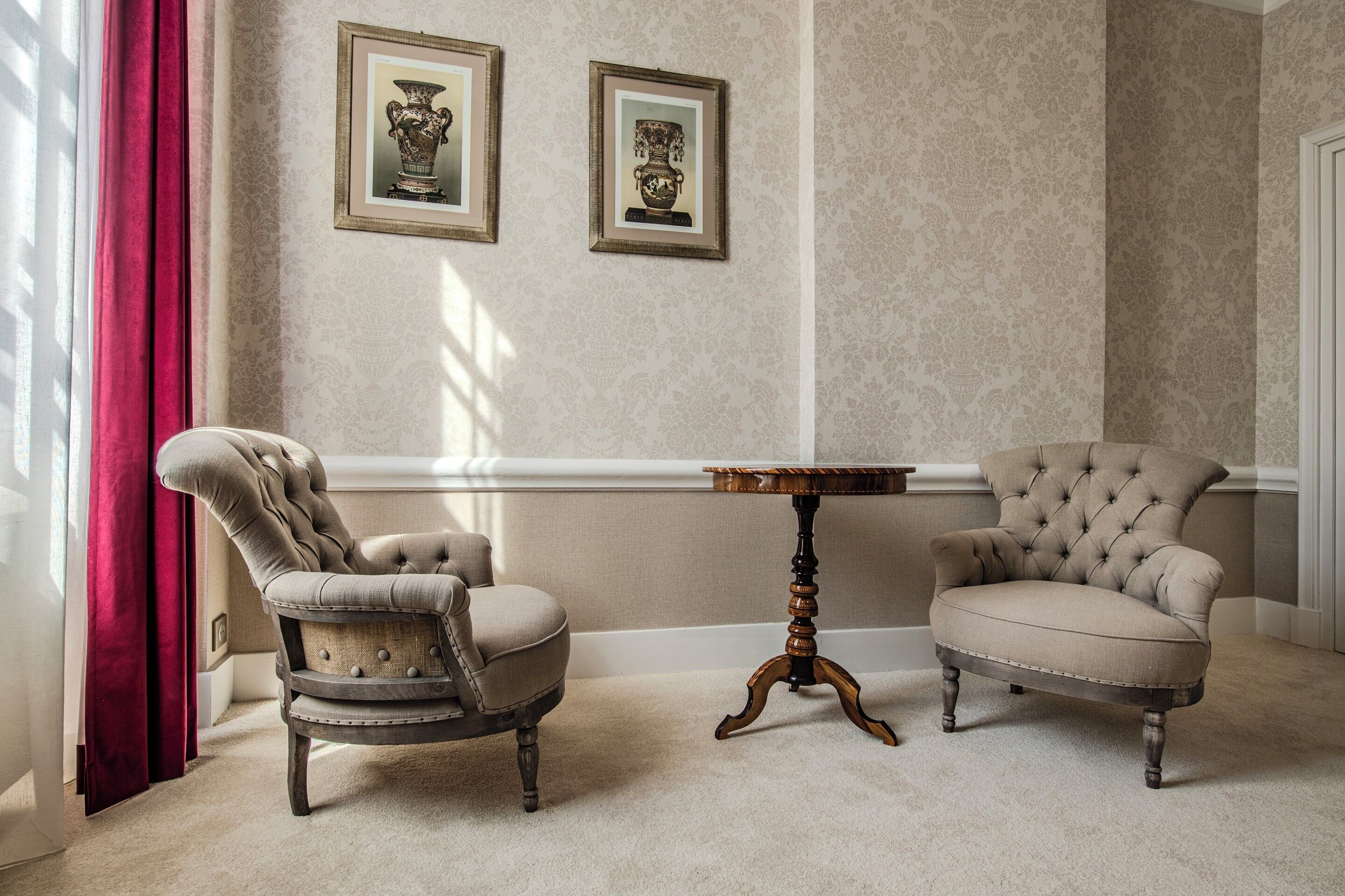 Een kamer met twee gestoffeerde fauteuils, een klein houten tafeltje en twee lijstwerken met vazen aan de muur.