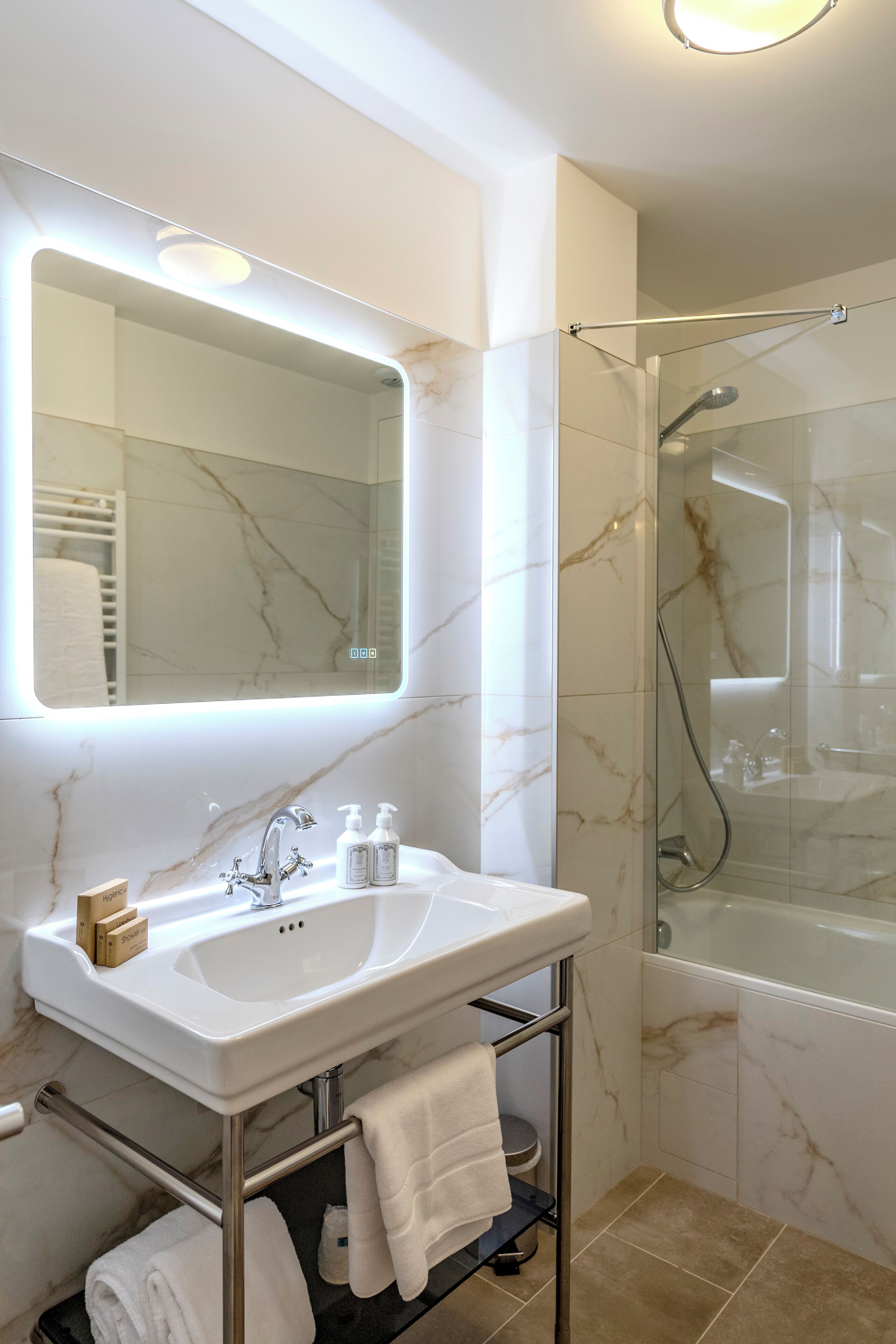 A modern bathroom with a marble sink, a glass-enclosed shower, and a large mirror with integrated lighting.
