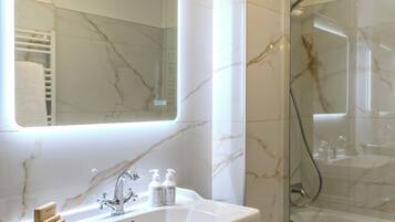 A modern bathroom with a marble sink, a glass-enclosed shower, and a large mirror with integrated lighting.