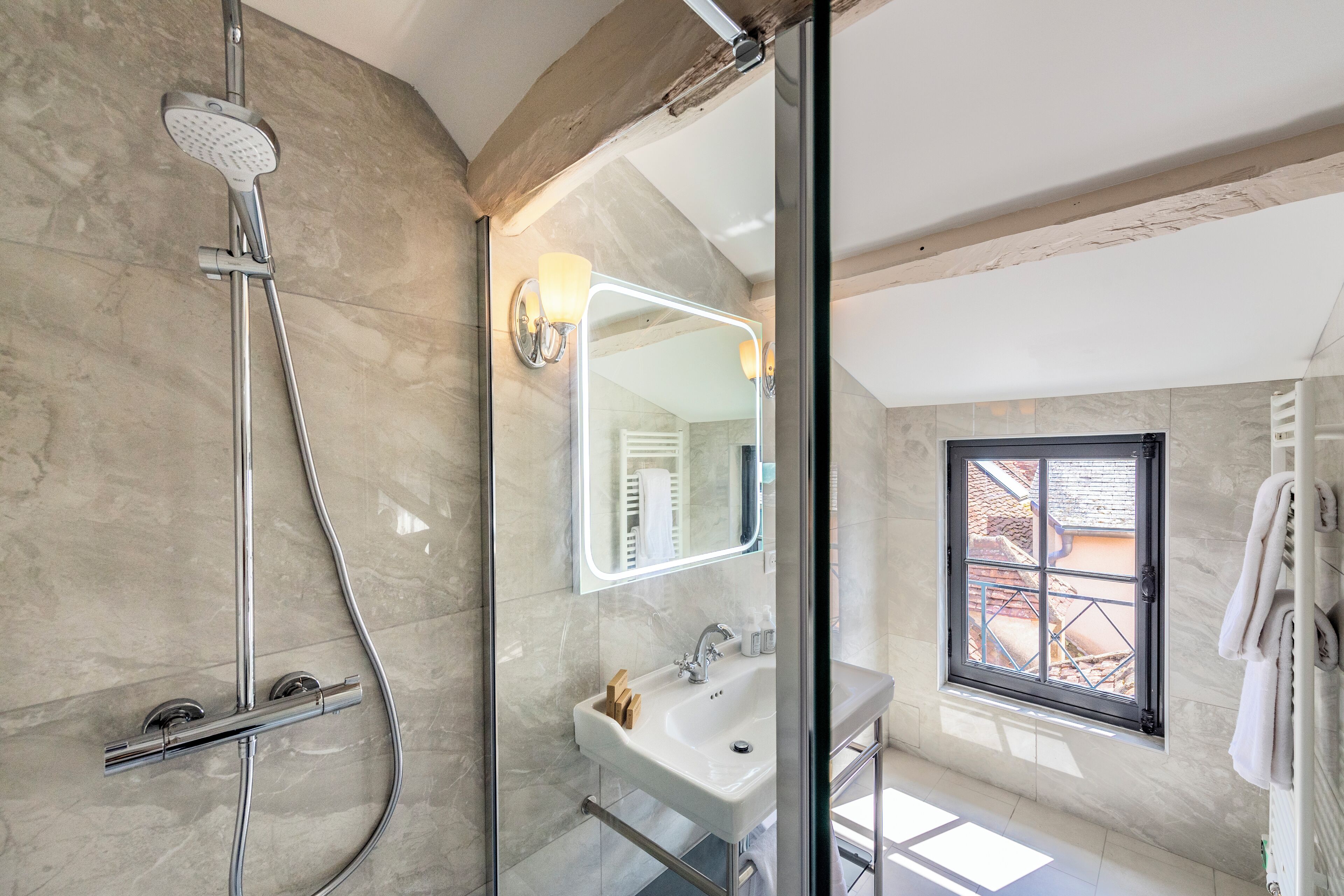 Un bagno moderno con doccia vetro, uno specchio grande, un lavandino e una finestra con vista esterna.