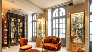 A luxurious room with a large window, a grand piano, and a collection of ornate furniture and glass display cases.