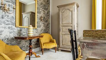 A room with a floral wallpaper, two yellow armchairs, a wooden cabinet, and a dining table with chairs.