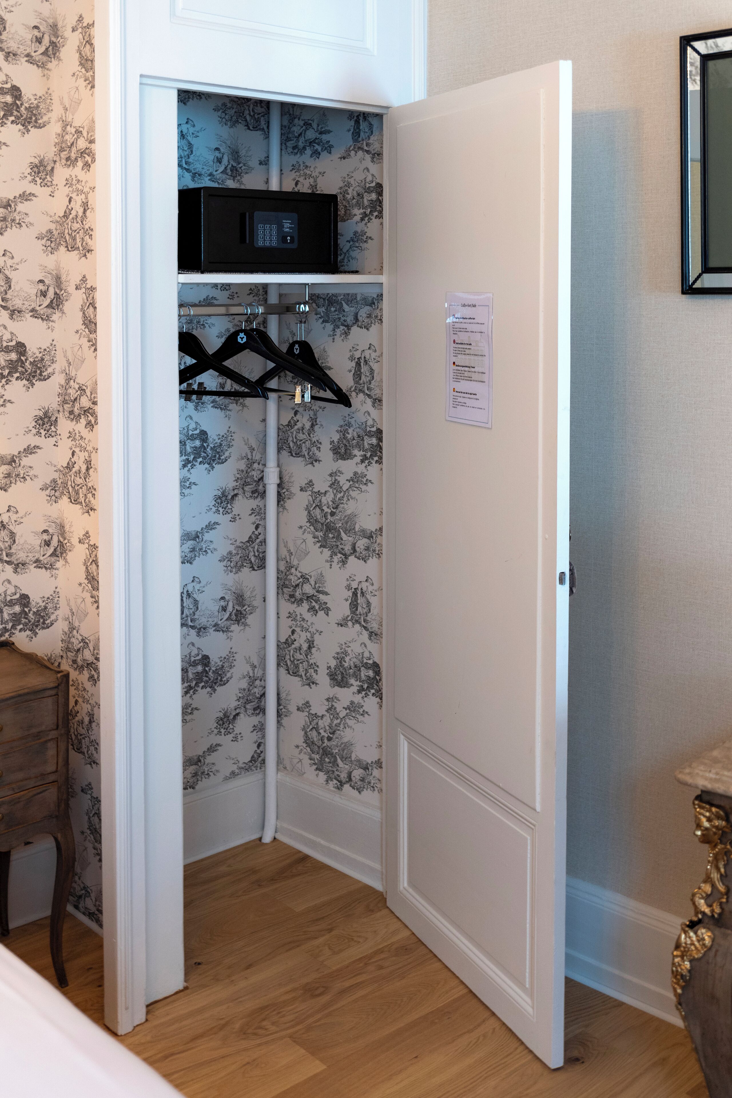 A corner room with a white door, a wooden dresser, a black microwave, and a clothing rack.