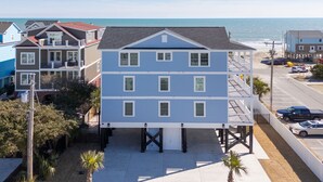 A multi-story building with a balcony on the second floor, situated near a beach with a clear view of the ocean.