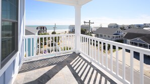 A covered balcony with a view of the beach and neighboring houses.