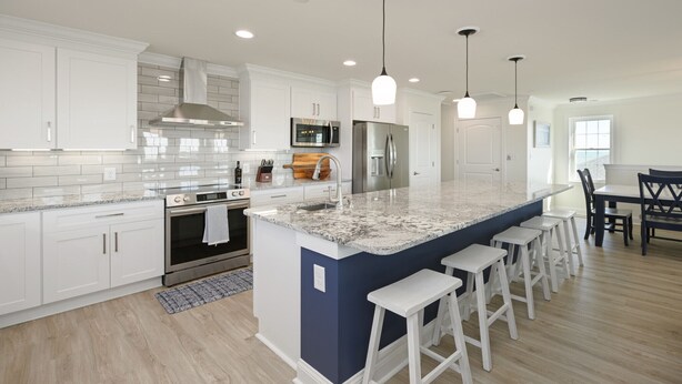 A modern kitchen with white cabinets, a stainless steel refrigerator, and a granite island with bar stools.
