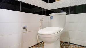 Et toilet i et badeværelse med hvide flisevægge og et mønstret gulv.