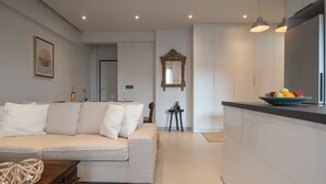 A modern living room with a sofa, a coffee table, and a kitchen area with a fruit bowl. - Pagrati Urban Living  (Athens)