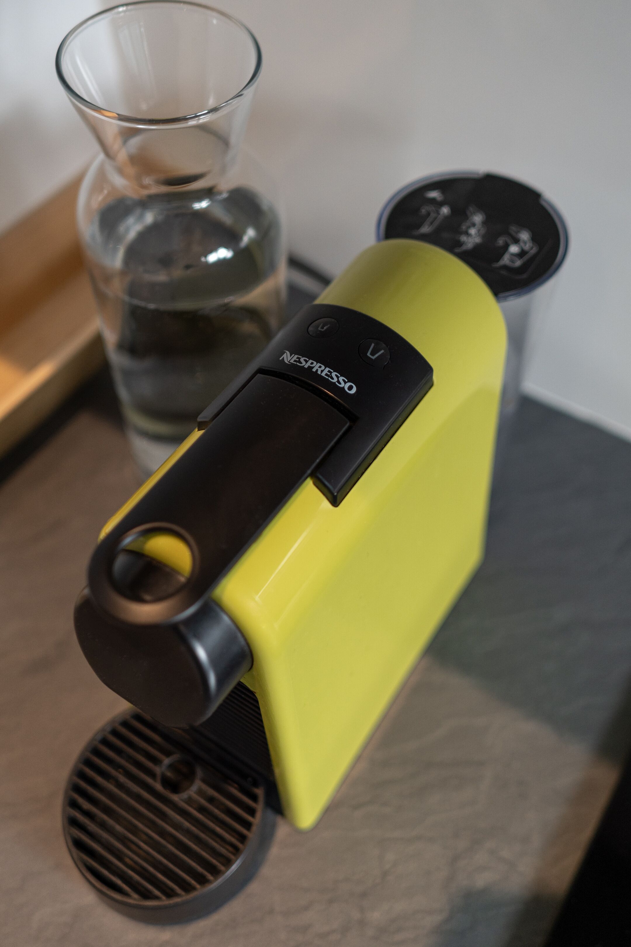 A yellow espresso machine with a black control panel and a glass of water nearby.