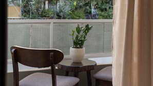 A balcony with a wooden chair and a small table, a potted plant, and a view of a garden and building. - Pagrati Urban Living  (Athens)