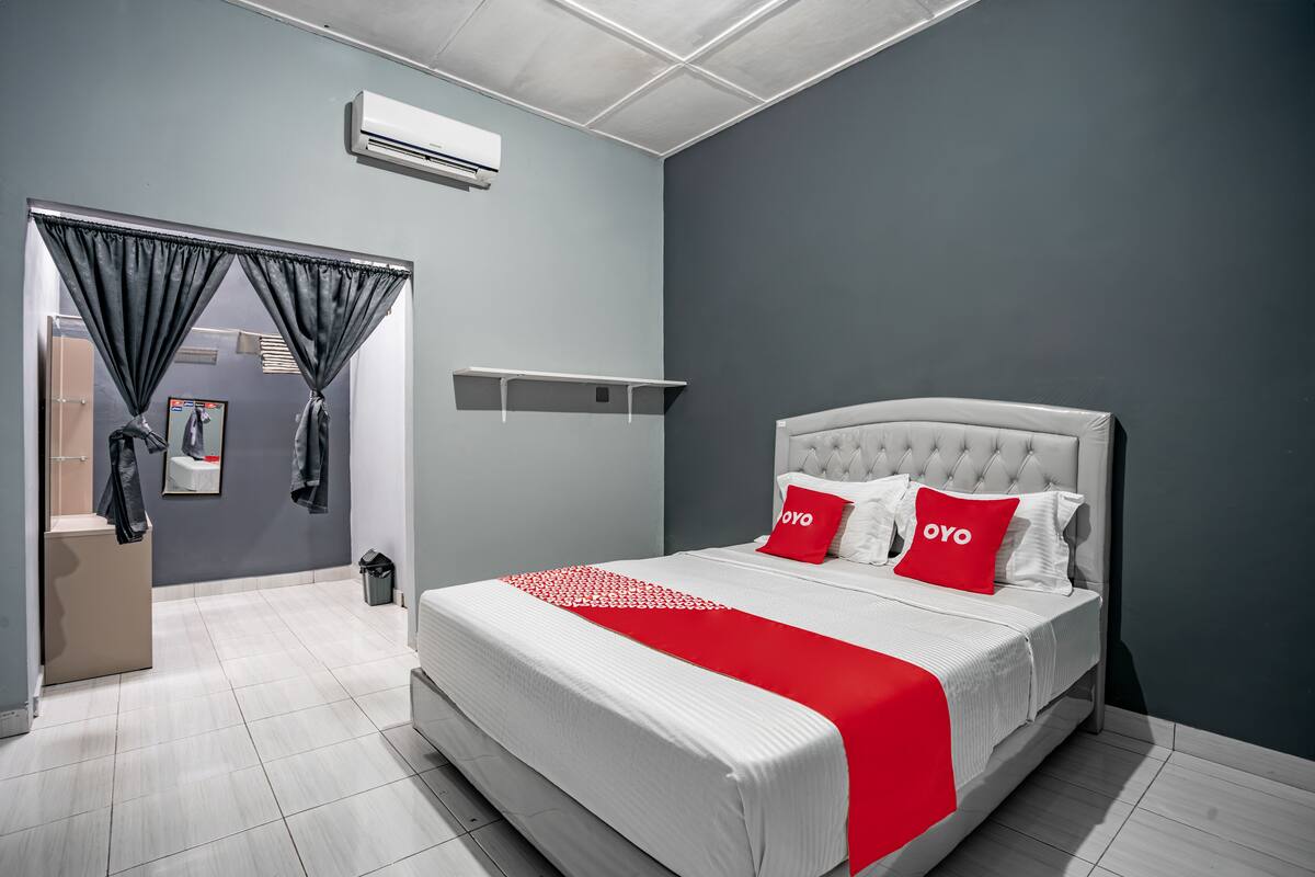Un dormitorio moderno con una cama grande, paredes grises y un detalle en rojo.
