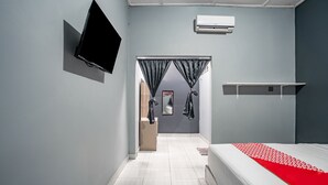 A modern bedroom with a bed, a TV mounted on the wall, and a small shelf.