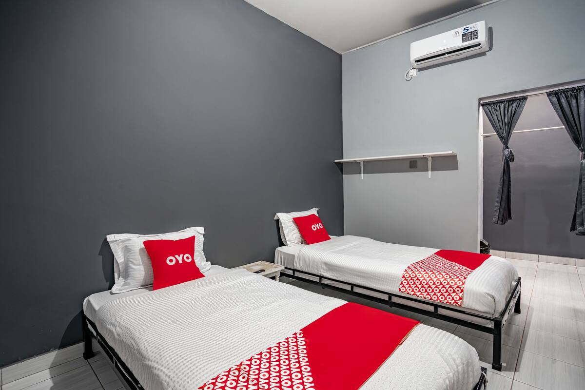 Habitación de hotel con dos camas, paredes grises, un equipo de aire acondicionado y una ventana con cortinas.