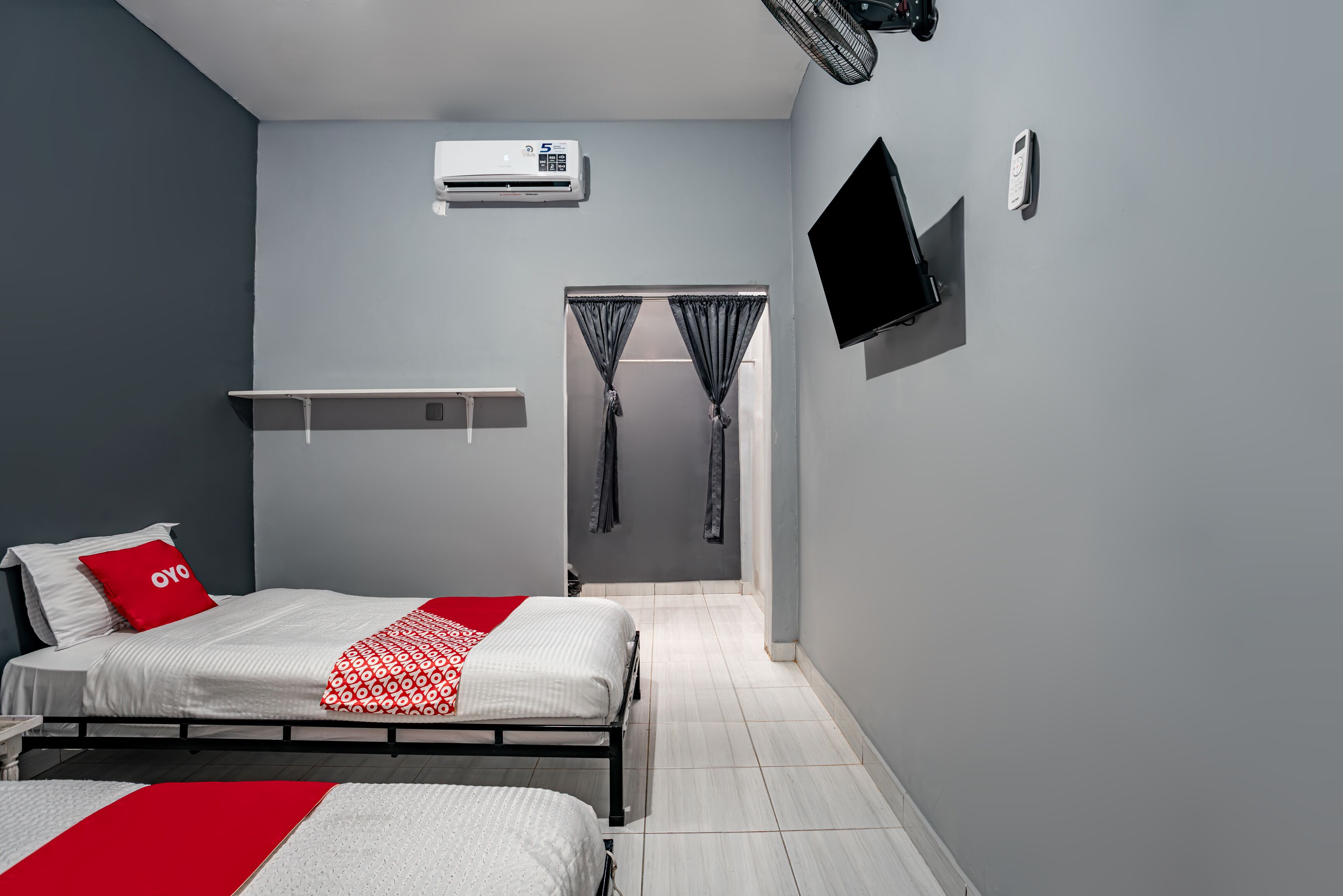 A modern bedroom with a bed, a TV, an air conditioning unit, and a small shelf.