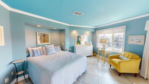 A bedroom with a bed, a yellow armchair, a dresser, a vanity, and a window with a view. - Spectacular Penthouse Oasis with Mesmerizing Ocean Views (Isle of Palms)
