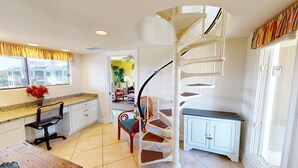 A kitchen with a spiral staircase, a dining area with a chair and table, and a view of a yellow room through an open door. - Spectacular Penthouse Oasis with Mesmerizing Ocean Views (Isle of Palms)