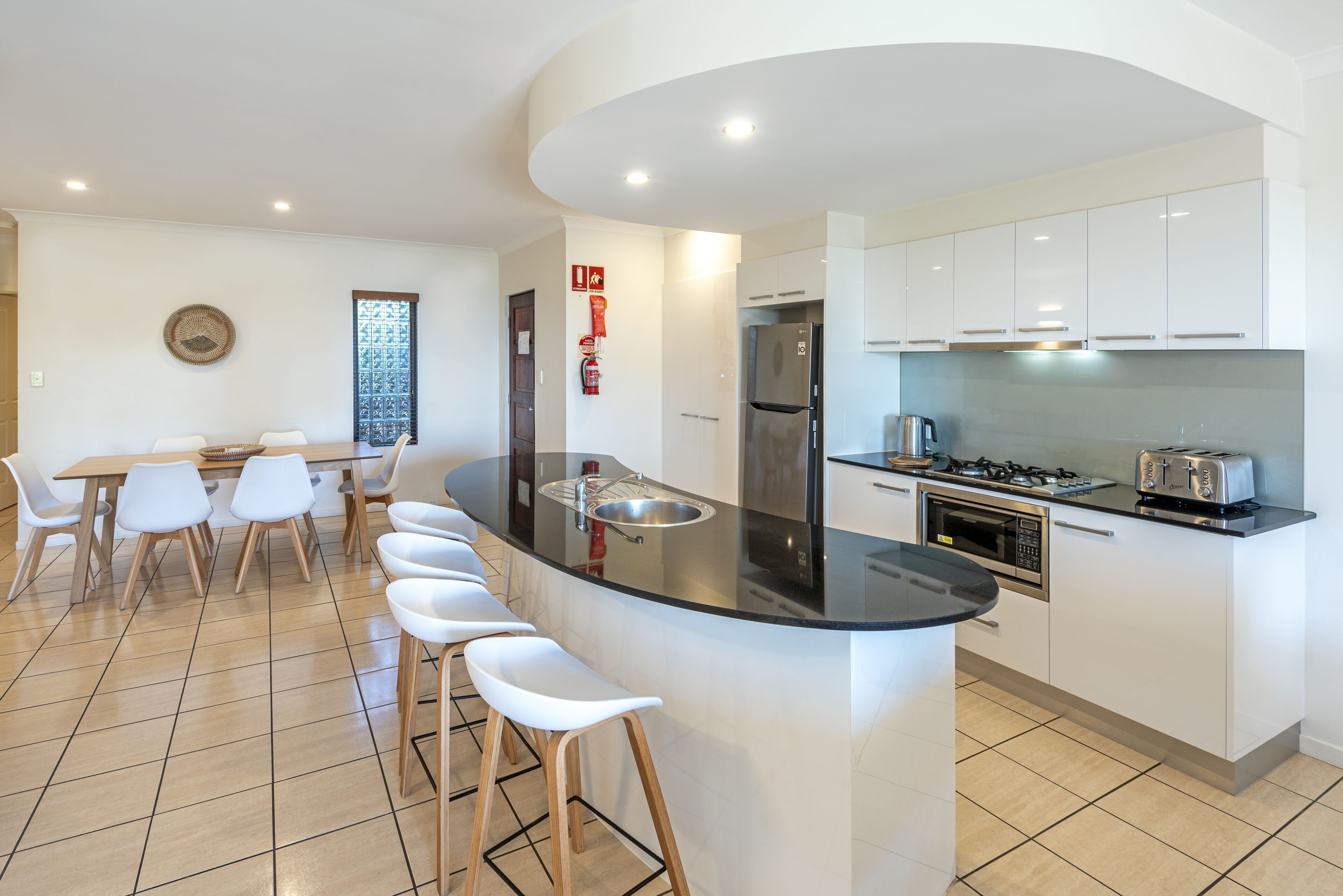 Une cuisine moderne avec des meubles blancs, un îlot central doté de tabourets, un four encastré et un four à micro-ondes.