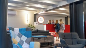 A reception area with a modern design, featuring a reception desk, a clock, and a seating area with a couch and chairs. - Athens Hawks Urban (Athens)