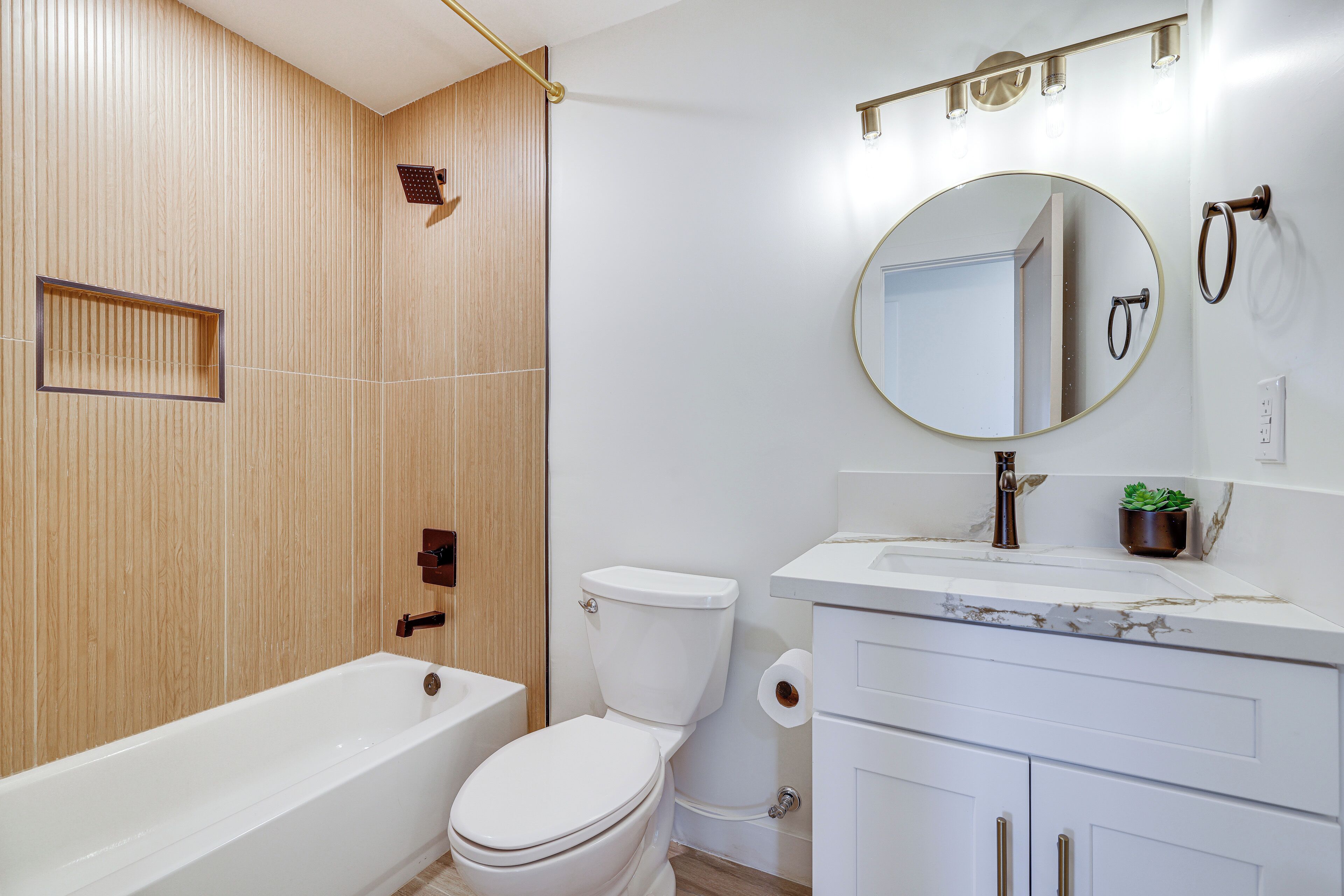A modern bathroom with a bathtub, toilet, vanity, and a mirror.