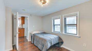 Quarto com cama, duas janelas e porta para um banheiro.