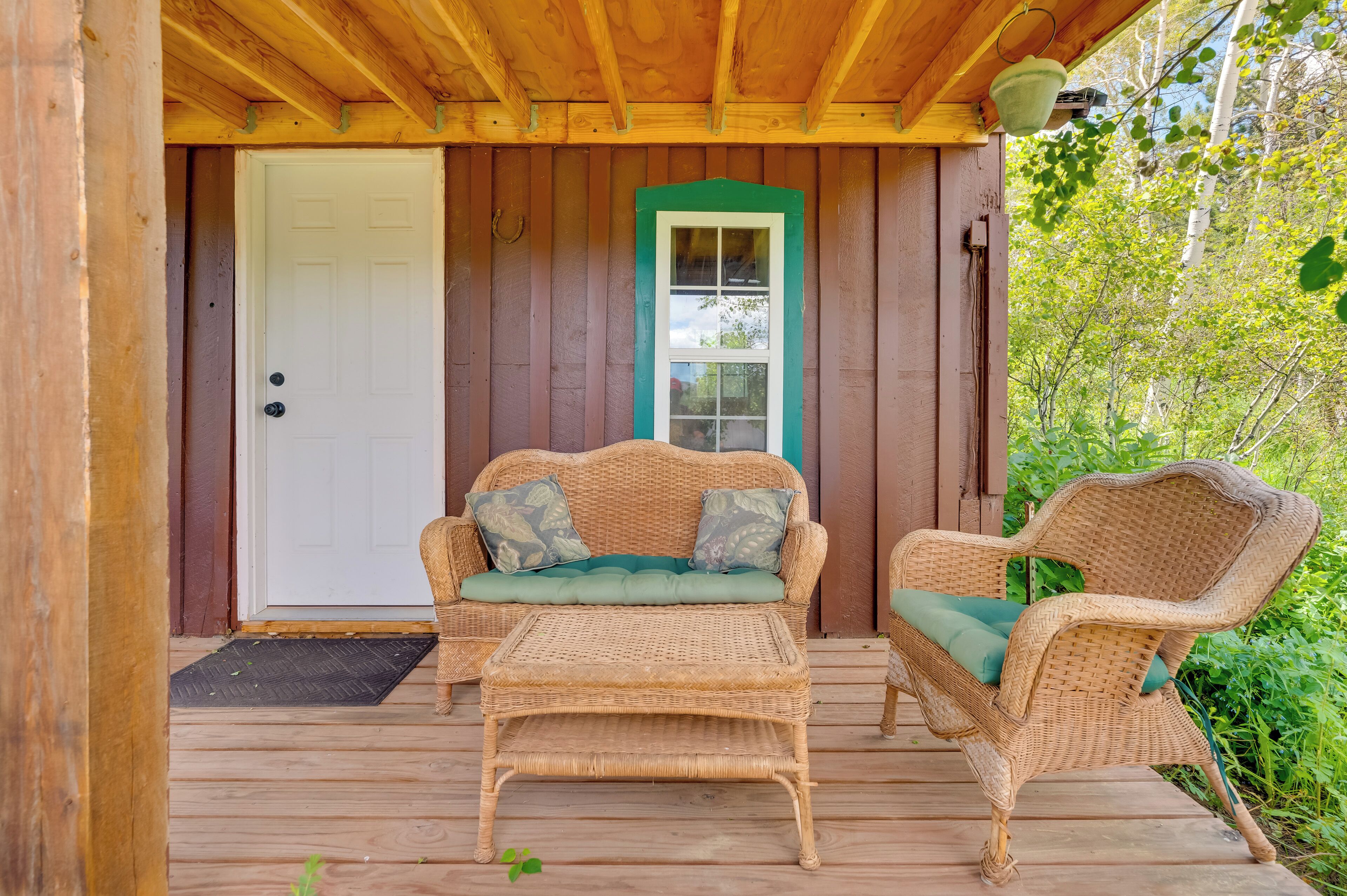 A wooden porch with wicker furniture, a white door, and a green-framed window.