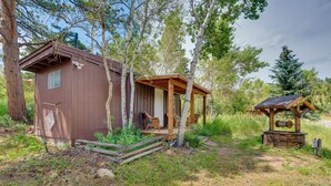 Eine rustikale Holzhütte mit Veranda, umgeben von Bäumen und einer kleinen Sitzgelegenheit im Freien.