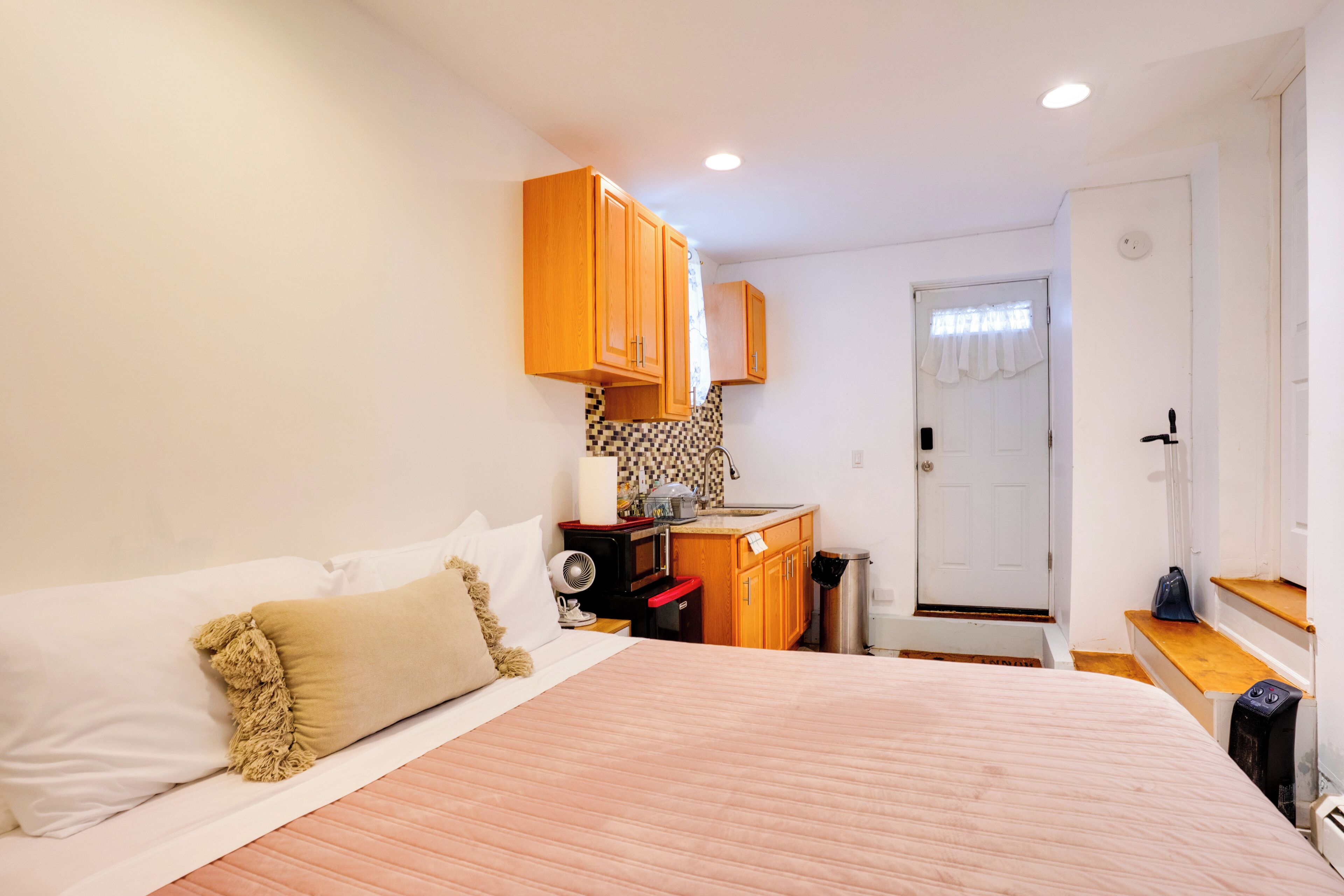 A bedroom with a bed, a small kitchenette, and a door leading to another room.