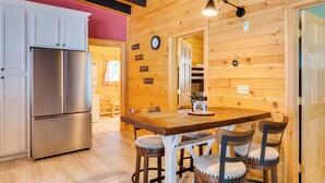 Una cocina con un refrigerador de acero inoxidable, paredes de madera, una mesa de comedor de madera con cuatro sillas y un reloj en la pared.