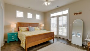 A bedroom with a bed, nightstands, a ceiling fan, a large mirror, and a window with blinds.