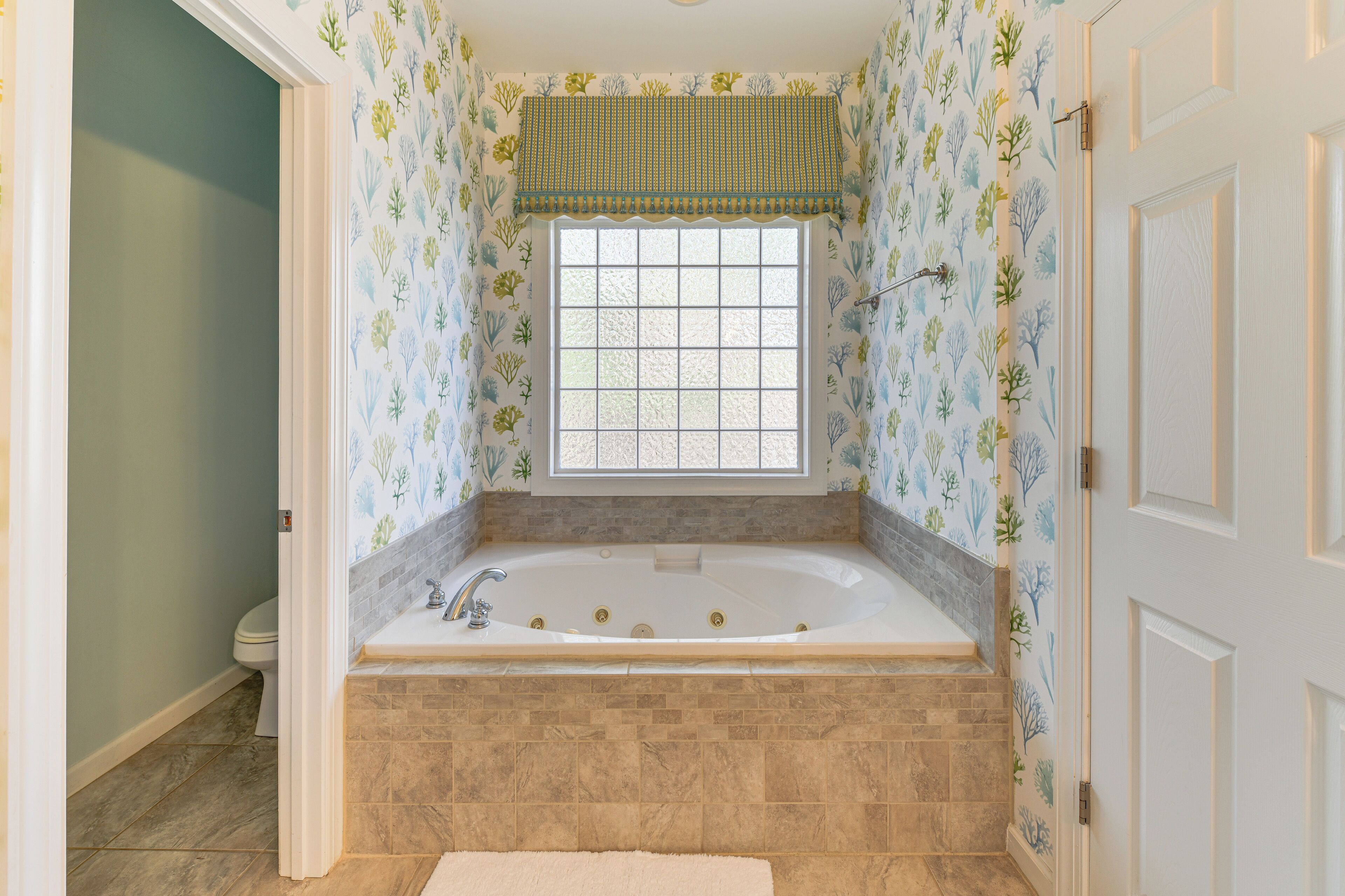 A bathroom with a freestanding bathtub, a window with a decorative valance, and patterned wallpaper.