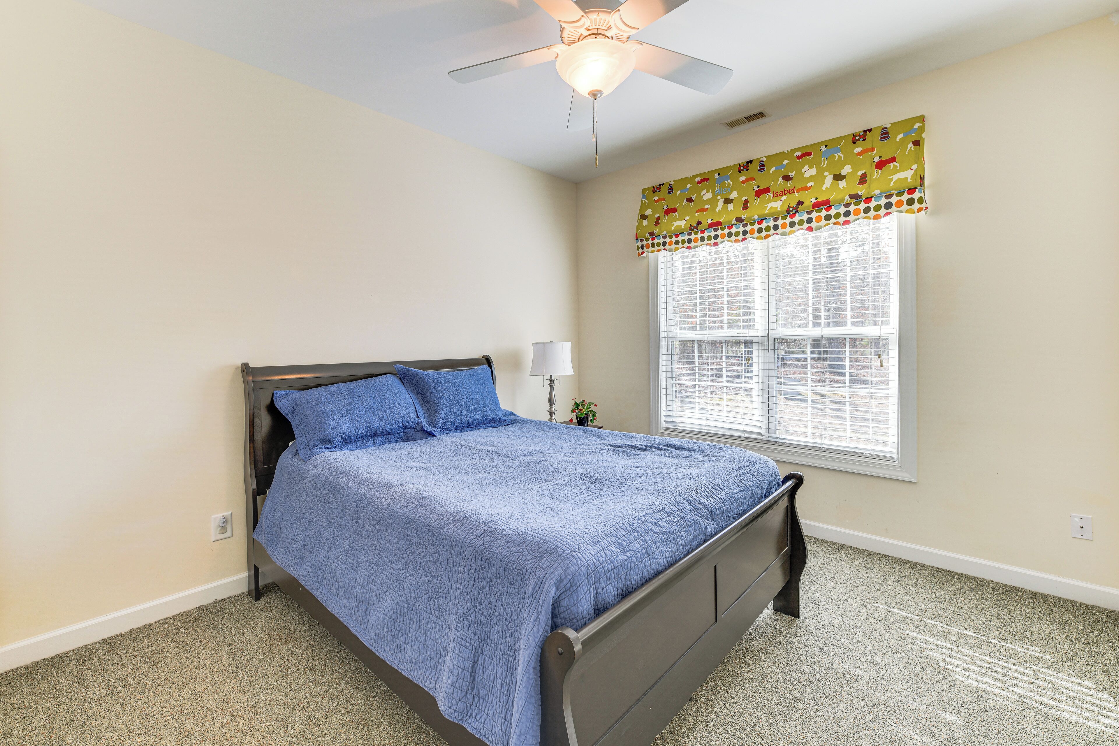 A bedroom with a bed, a ceiling fan, a window with blinds, and a wall-mounted lamp.