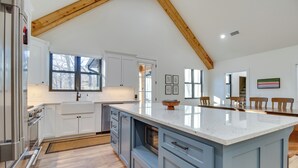 A modern kitchen with white cabinets, a large island, and wooden beams on the ceiling. - Waterfront Flippin Retreat w/ White River Access! (Flippin)