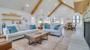 A spacious living area with a high ceiling, wooden beams, a fireplace, and a cozy seating arrangement. - Waterfront Flippin Retreat w/ White River Access! (Flippin)