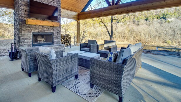 An outdoor patio with wicker furniture, a stone fireplace, and a large TV screen. - Waterfront Flippin Retreat w/ White River Access! (Flippin)