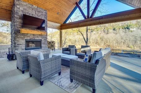 An outdoor patio with wicker furniture, a stone fireplace, and a large TV screen.