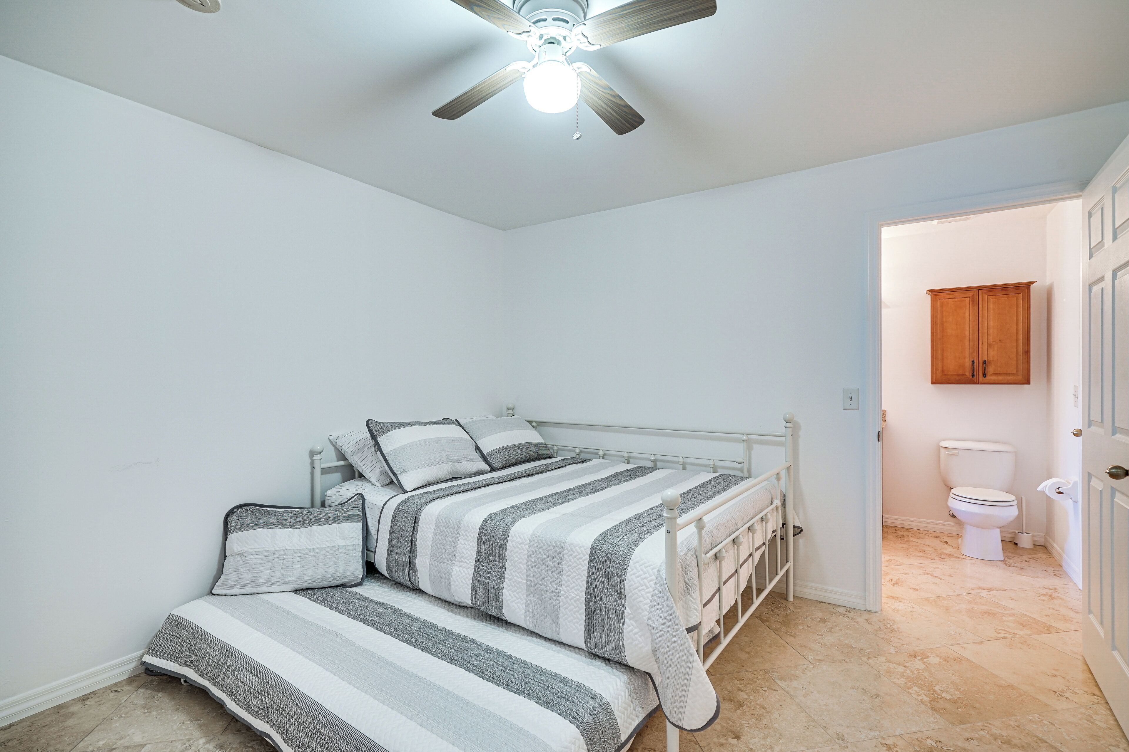Un dormitorio con cama, ventilador de techo y baño con inodoro y armario.