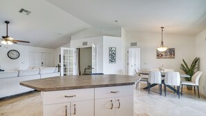 A spacious kitchen with a large island, white cabinetry, and a dining area with a table and chairs. - Canal-front Cape Coral Home w/ Fire Pit, By Beach! (Cape Coral)