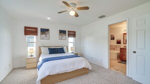 A bedroom with a bed, a ceiling fan, a nightstand, a window with blinds, and a door leading to a bathroom. - Canal-front Cape Coral Home w/ Fire Pit, By Beach! (Cape Coral)