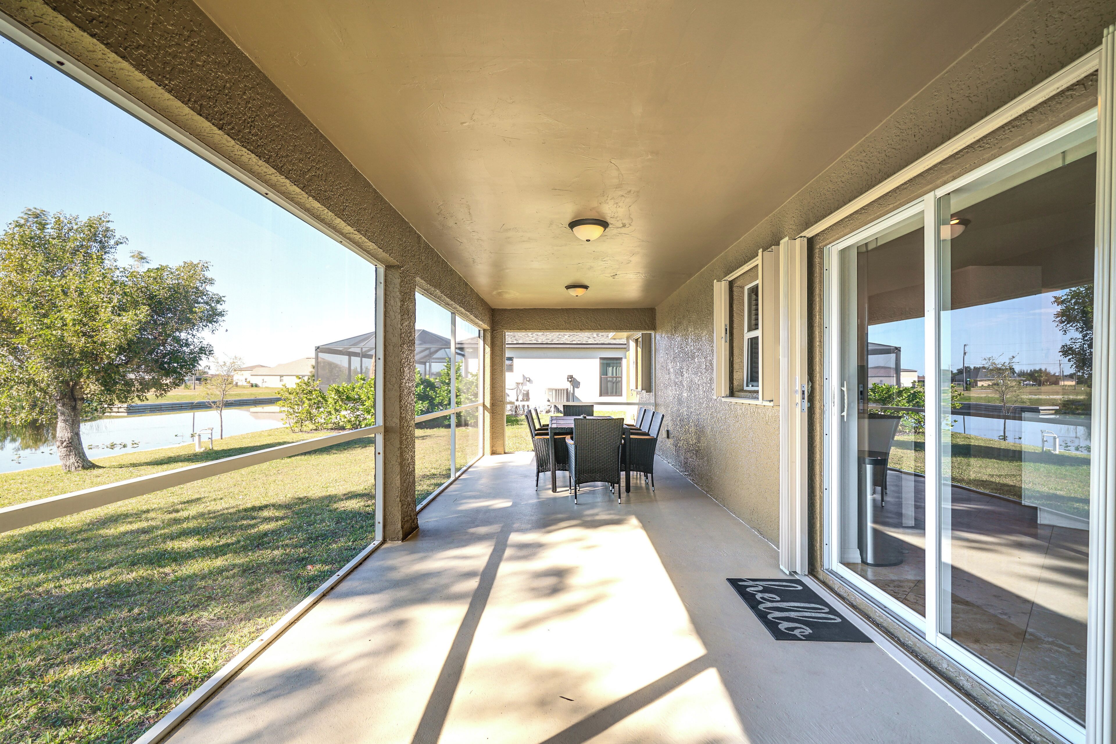 A covered patio area with a table and chairs, large windows, and a view of a lake.