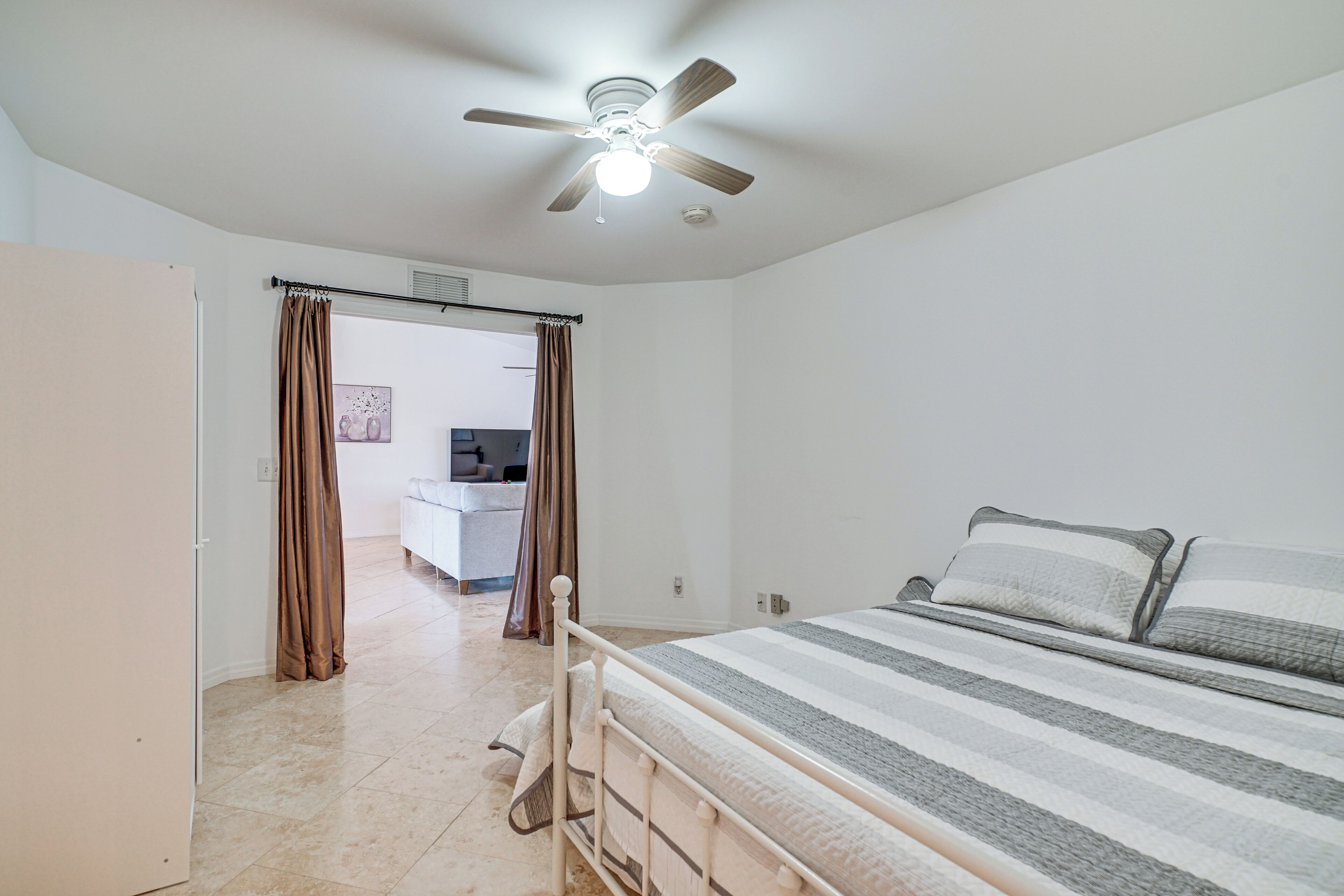 Ein Schlafzimmer mit Bett, Deckenventilator und Blick in einen weiteren Raum.