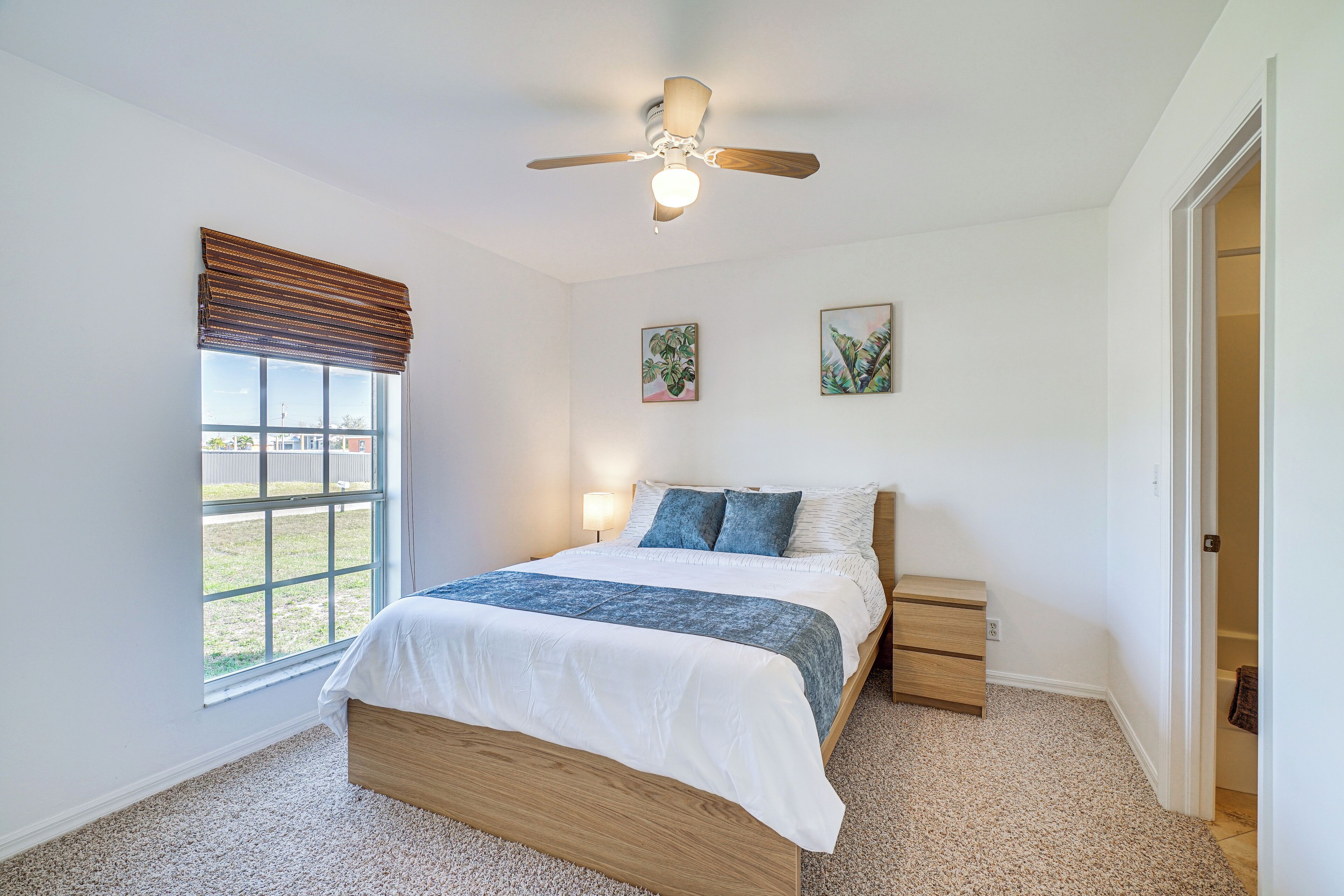 Ein Schlafzimmer mit einem Bett, einem Deckenventilator, einem Fenster mit Jalousien und zwei Bildern an der Wand.