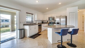 A modern kitchen with white cabinets, stainless steel appliances, and a large island with bar stools. - Canal-front Cape Coral Home w/ Fire Pit, By Beach! (Cape Coral)